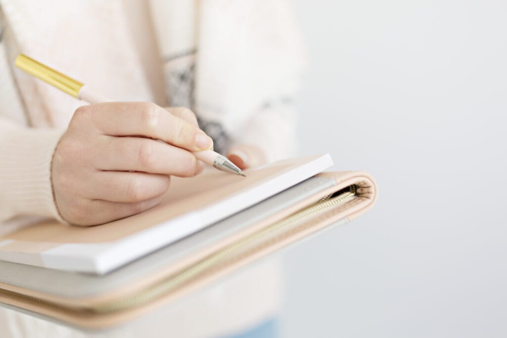 Woman wearing a cozy cream sweater holding a journal and writing with a pen