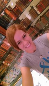 Gabe Cox smiling at the camera while standing in front of a wall of books