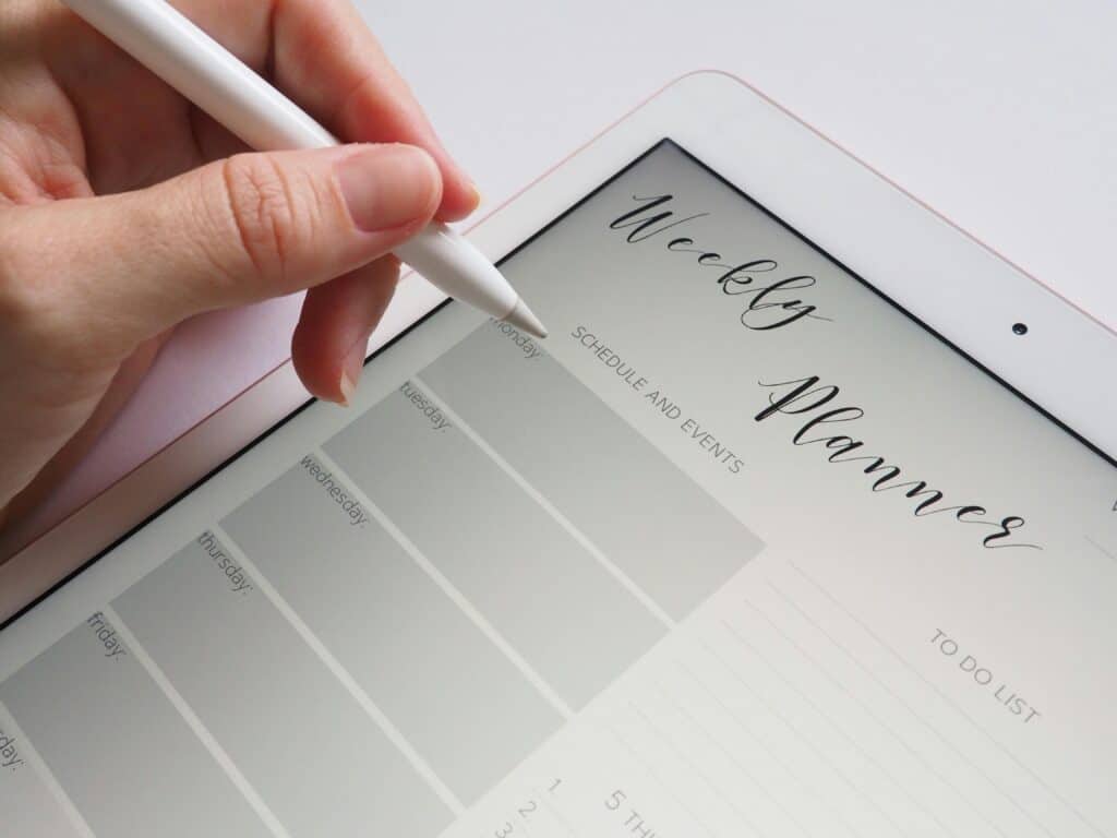 a weekly planner pulled up on an ipad with a hand and stylist working