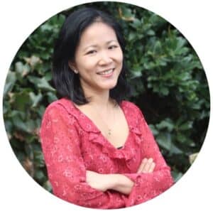 Headshot of woman with medium black hair smiling wearing a pink, floral blouse with arms crossed in front of her