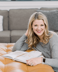 Headshot of Polly Payne from Horacio Printing smiling with medium blonde, wavy hair sitting on the floor, leaning on an ottoman with a journal open.